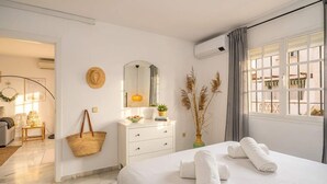 A hotel room with a bed, a dresser, a mirror, a window with curtains, and a view of the outside. - Beachfront Apartment w/ Pool & Golf Access - La Duquesa (Málaga)