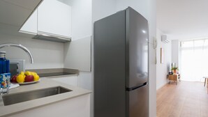 Cozinha moderna com geladeira de aço inoxidável, pia com torneira e bancada com frutas.