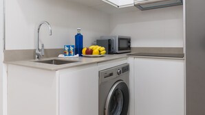 Uma cozinha compacta com máquina de lavar, micro-ondas e pia.