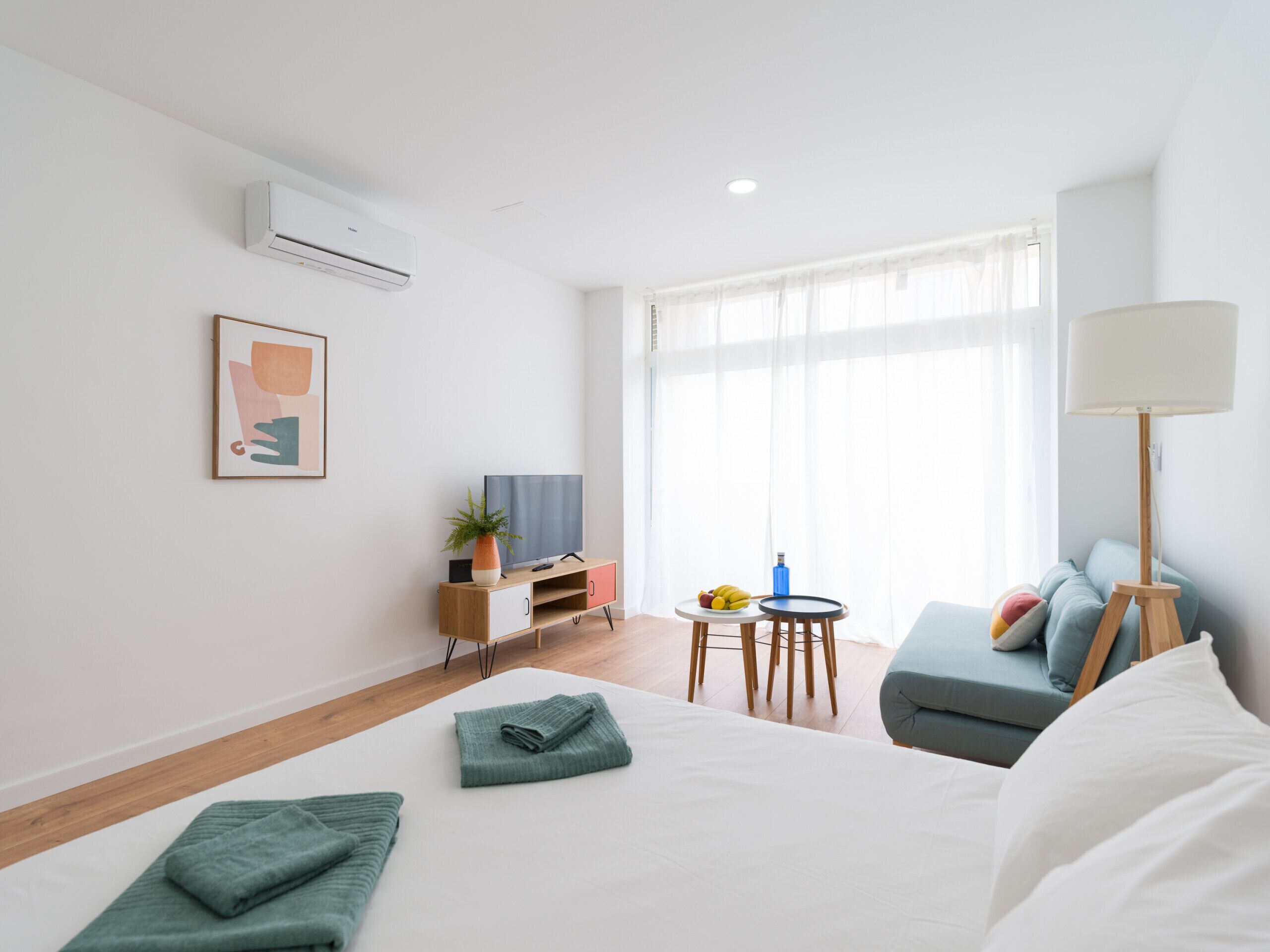A modern hotel room with a bed, a desk, a chair, a small table, and a sofa.