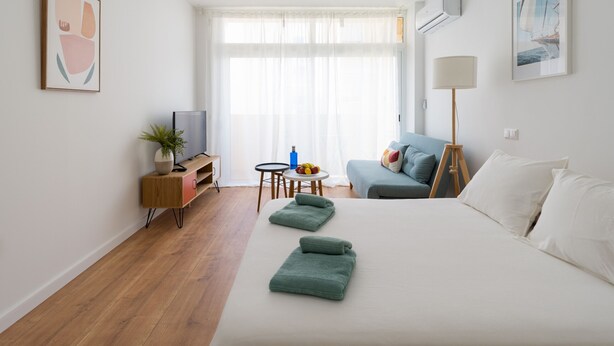 A modern hotel room with a bed, a desk, a sofa, and a TV. - HomeForGuest Studio Sol Canteras with terrace  (Las Palmas de Gran Canaria)