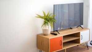 A wooden TV stand with a flat-screen TV, a potted plant, and a remote control. - HomeForGuest Studio Sol Canteras with terrace  (Las Palmas de Gran Canaria)