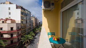 A balcony with a table and chairs, overlooking a street lined with palm trees and buildings. - HomeForGuest Studio Sol Canteras with terrace  (Las Palmas de Gran Canaria)