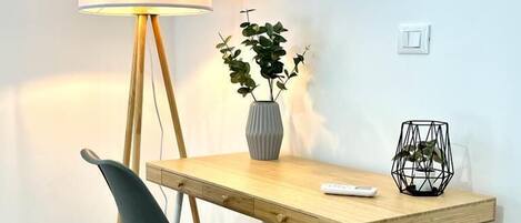 Un escritorio moderno con una silla, una lámpara, un florero con plantas y un espejo montado en la pared.
