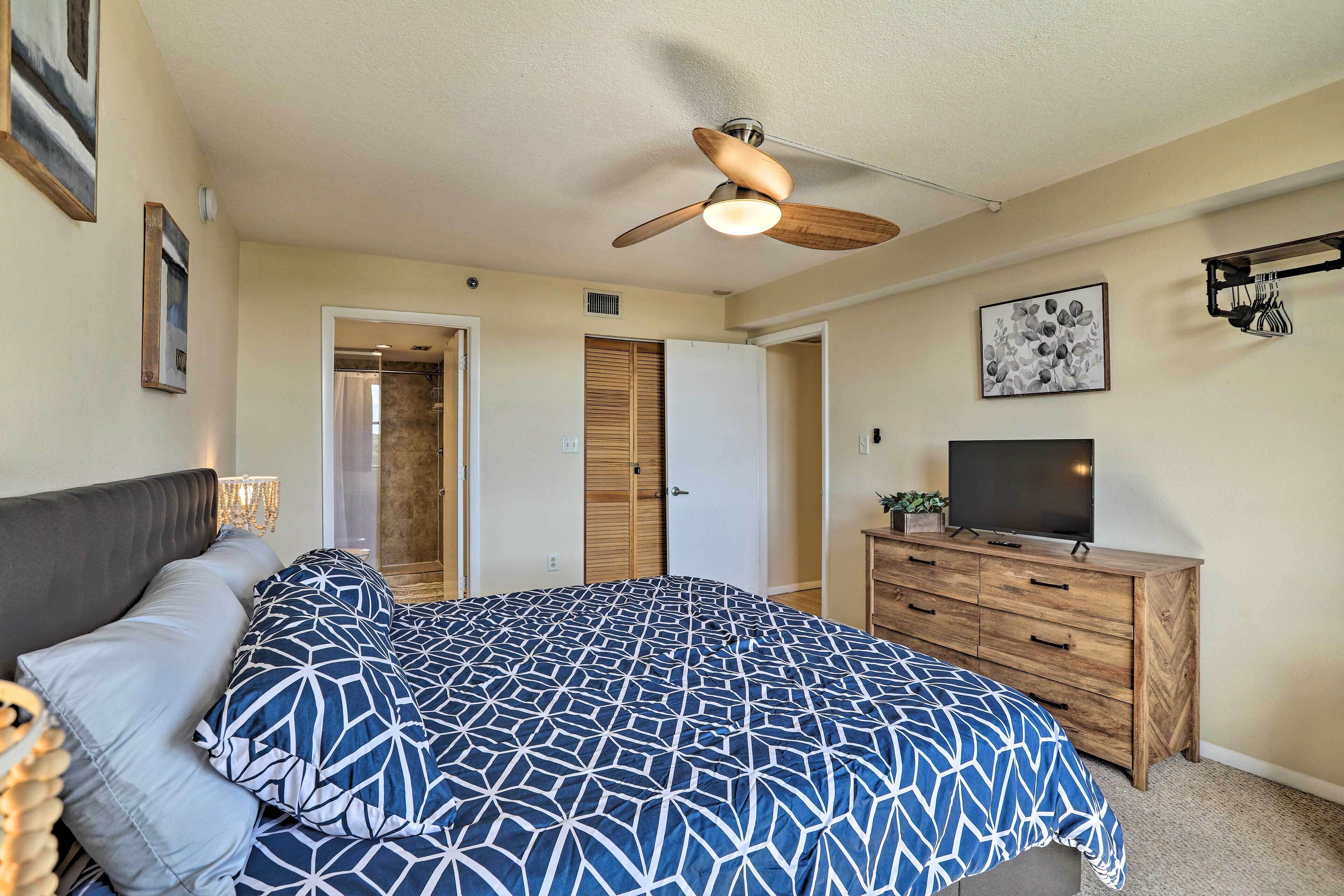 Un dormitorio con cama, ventilador de techo, cómoda, televisor y una puerta.