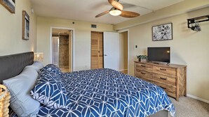 Une chambre à coucher avec un lit, un ventilateur de plafond, une commode, un téléviseur et une porte.