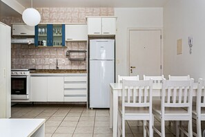 A compact kitchen with white cabinets, a Bosch oven, a refrigerator, and a dining area with white chairs.