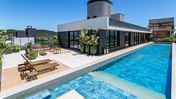 A modern building with a swimming pool, outdoor seating, and a view of the surrounding area. - WI-FI 300MB | Rooftop with Pool in Jurerê #JA15 (Florianópolis)