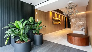 A modern lobby with a wooden wall, a large potted plant, a round wooden table, and a chandelier. - WI-FI 300MB | Rooftop with Pool in Jurerê #JA15 (Florianópolis)
