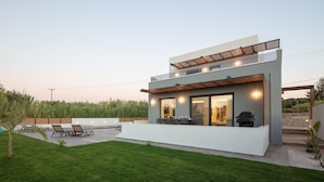 A modern two-story house with a flat roof, large windows, and a patio area with outdoor furniture.