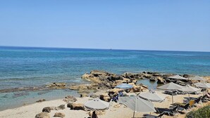 A beach with clear water, rocky shore, and umbrellas.