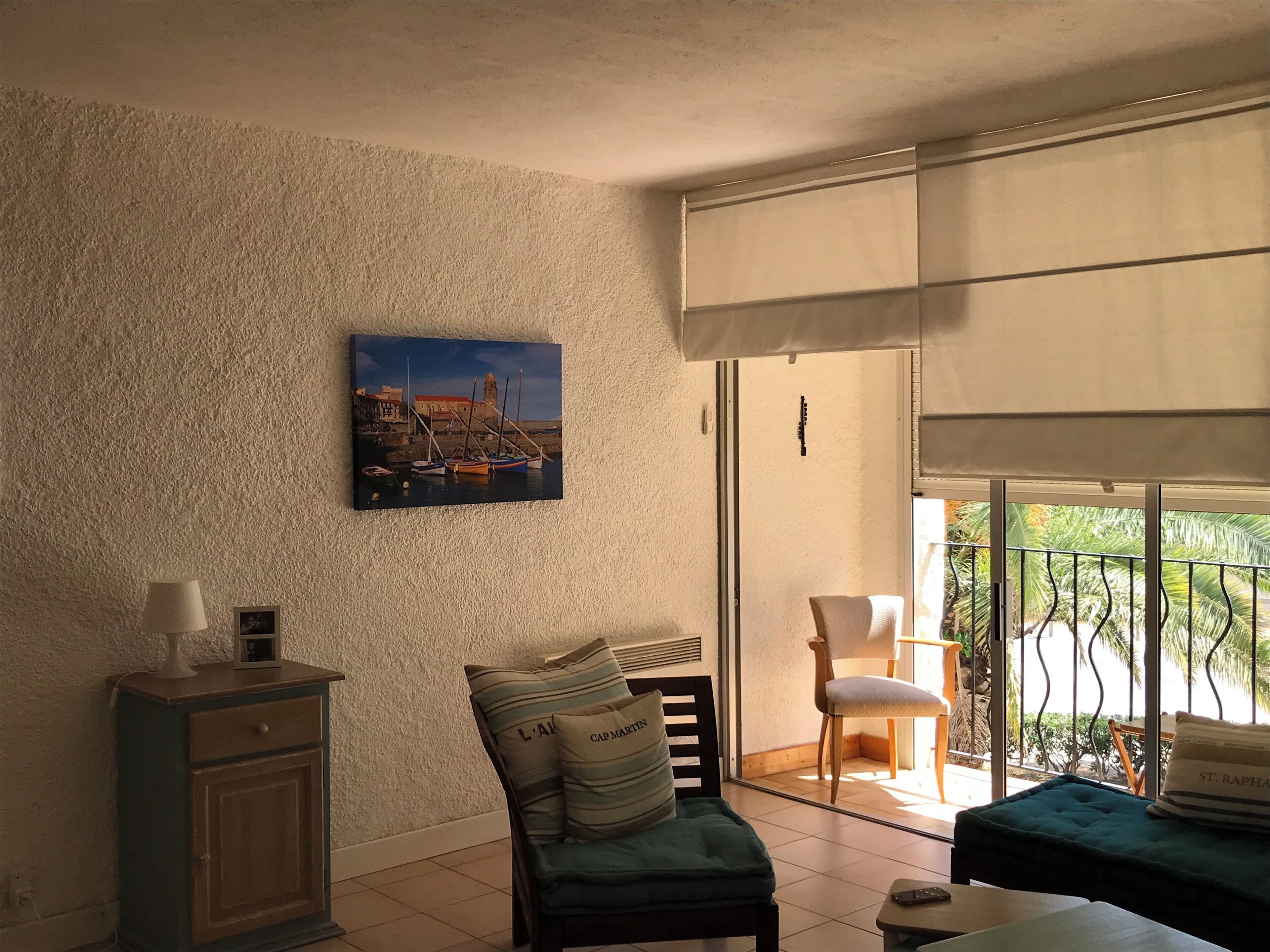 A room with a view of a harbor, a chair, a table, and a cabinet.