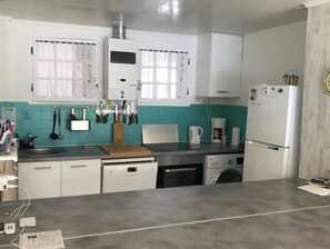 Eine Küche mit weißen Schränken, einem Herd, einem Spülbecken, einer Kaffeemaschine und einem Kühlschrank.