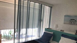 A bedroom with a bed, a window with sheer curtains, a view of the outdoors, and a painting on the wall. - A 200 M de la Plage (Argelès-sur-Mer)
