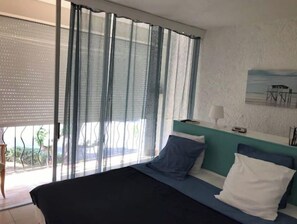 Ein Schlafzimmer mit Bett, einem Fenster mit durchsichtigen Vorhängen, Blick ins Freie und einem Bild an der Wand.