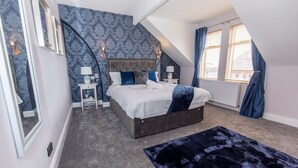 Ein Schlafzimmer mit einem großen Bett, einem dunkelblauen Teppich und einem Fenster mit Vorhängen.