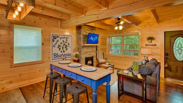 A wooden cabin interior with a dining table, bar stools, a fireplace, and a cozy seating area.