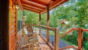 A wooden deck with rocking chairs and a view of a forested area.