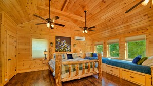 A wooden cabin interior with a bed, a bench, and a ceiling fan.