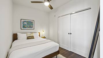 Quarto com cama, ventoinha no teto, mesa de cabeceira com abajur e guarda-roupa.