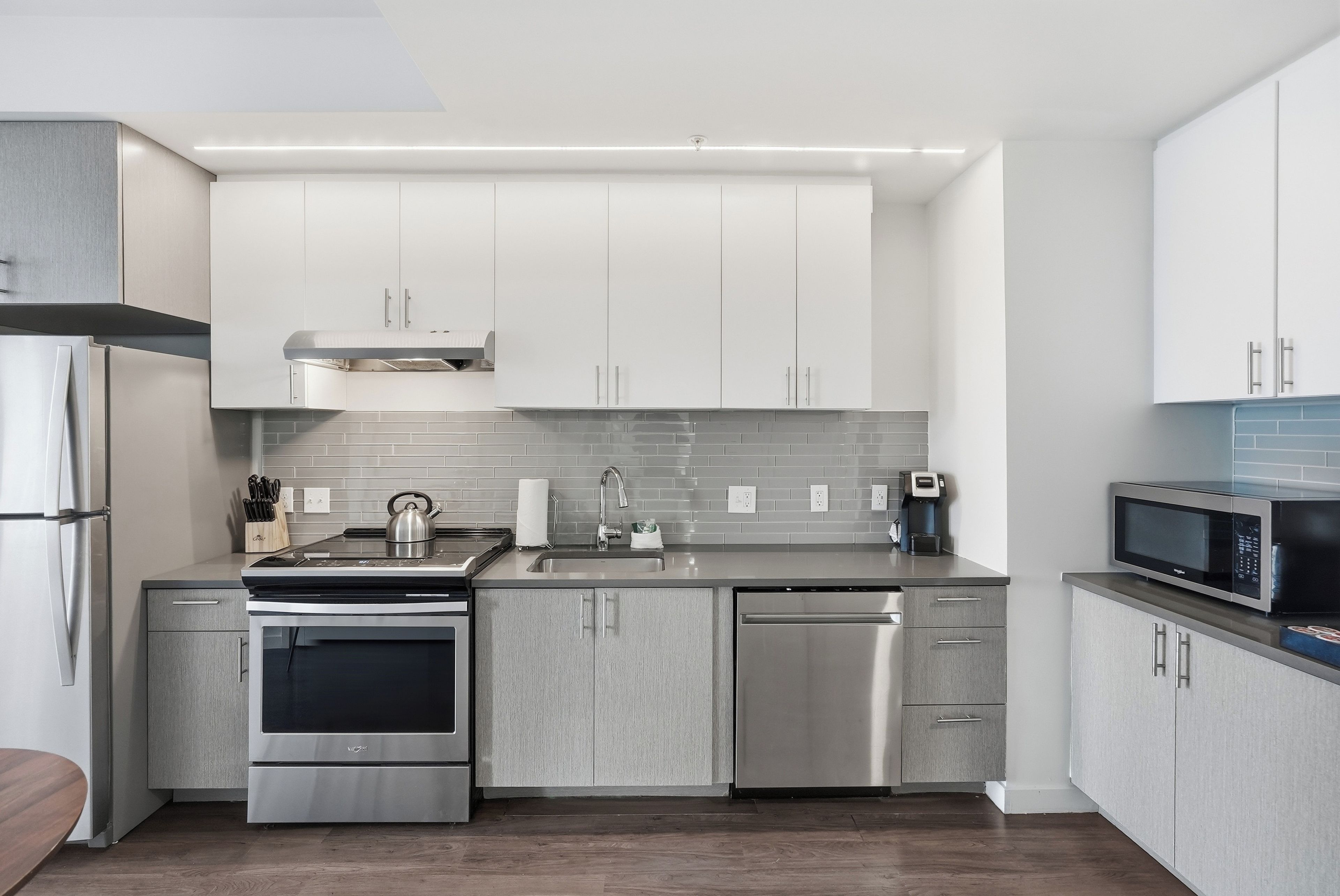 Une cuisine moderne dotée d’appareils électroménagers en acier inoxydable, de meubles de couleur grise et d’un pare-feu en carrelage.