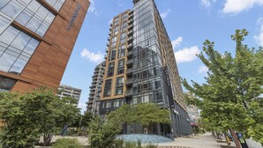A modern high-rise building with multiple balconies and large windows, surrounded by trees and a clear sky. - Placemakr Marymount Ballston (Arlington)