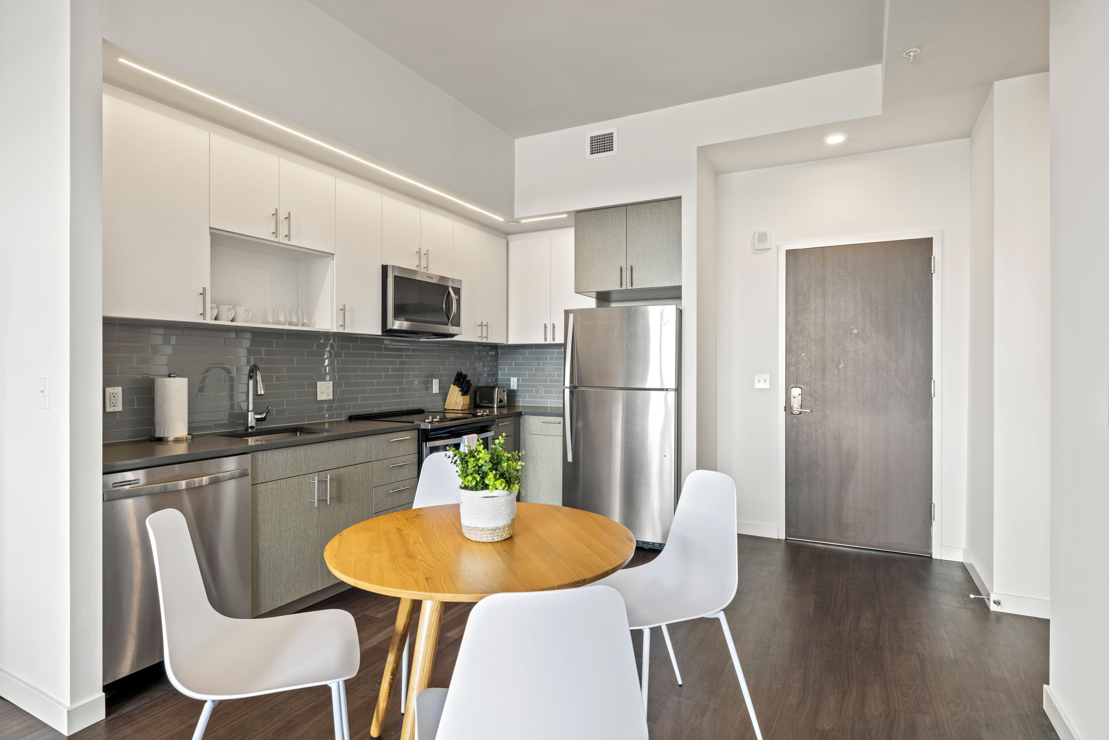 A modern kitchen with stainless steel appliances, white cabinetry, and a round wooden table with white chairs.