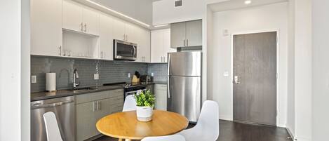 A modern kitchen with stainless steel appliances, white cabinetry, and a round wooden table with white chairs.