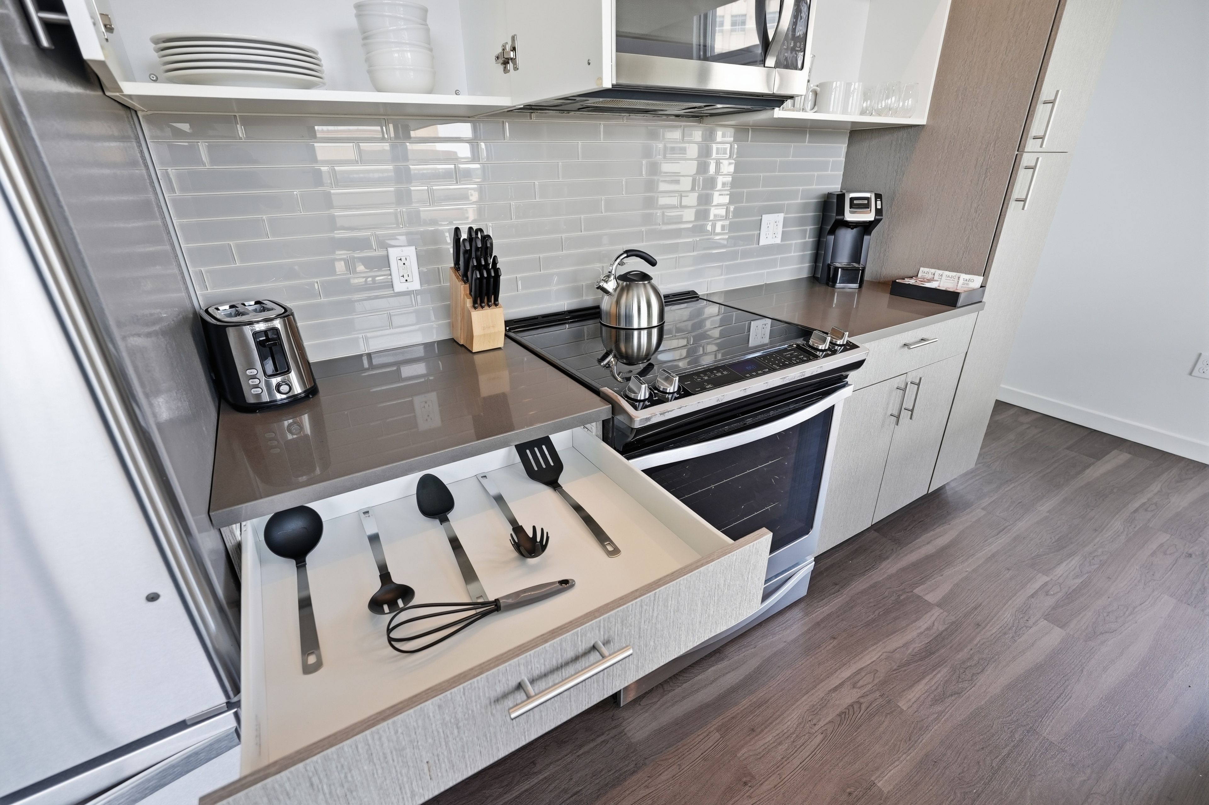 A modern kitchen with a stainless steel range, a kettle, a coffee maker, and a drawer with kitchen utensils.