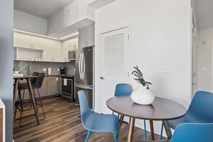 Una cocina moderna con armarios blancos, un refrigerador de acero inoxidable y un comedor con sillas azules y una mesa redonda.