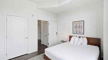 A hotel room with a large bed, a bedside table, a framed picture on the wall, and a door leading to another room.