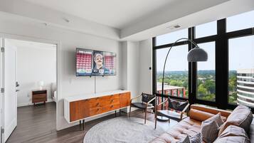 Una sala de estar moderna con un gran ventanal, un sofá, una mesa de centro, un televisor y vistas de la ciudad.
