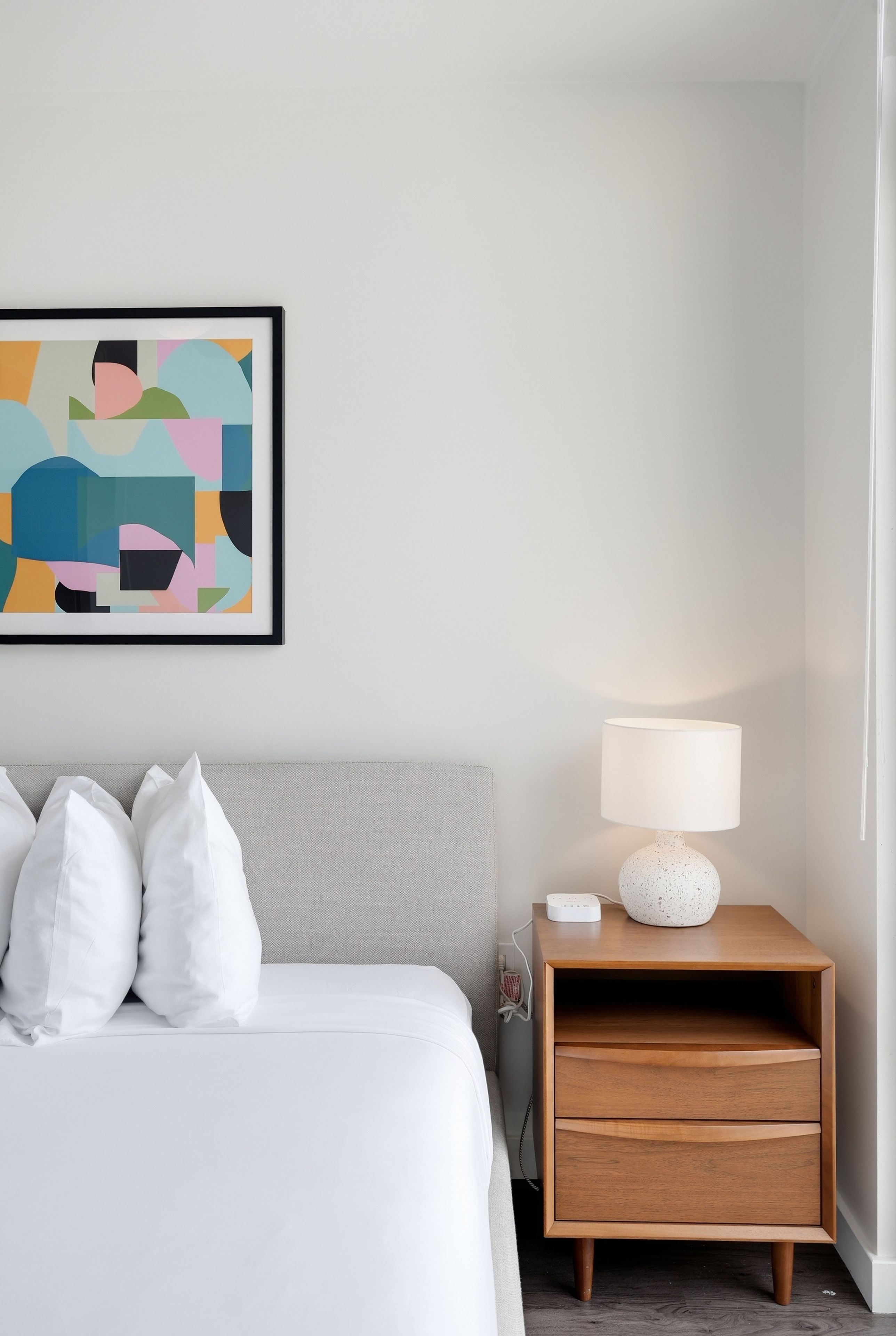 Une chambre à coucher avec un lit, des oreillers, une table de chevet avec une lampe et une œuvre d’art murale.