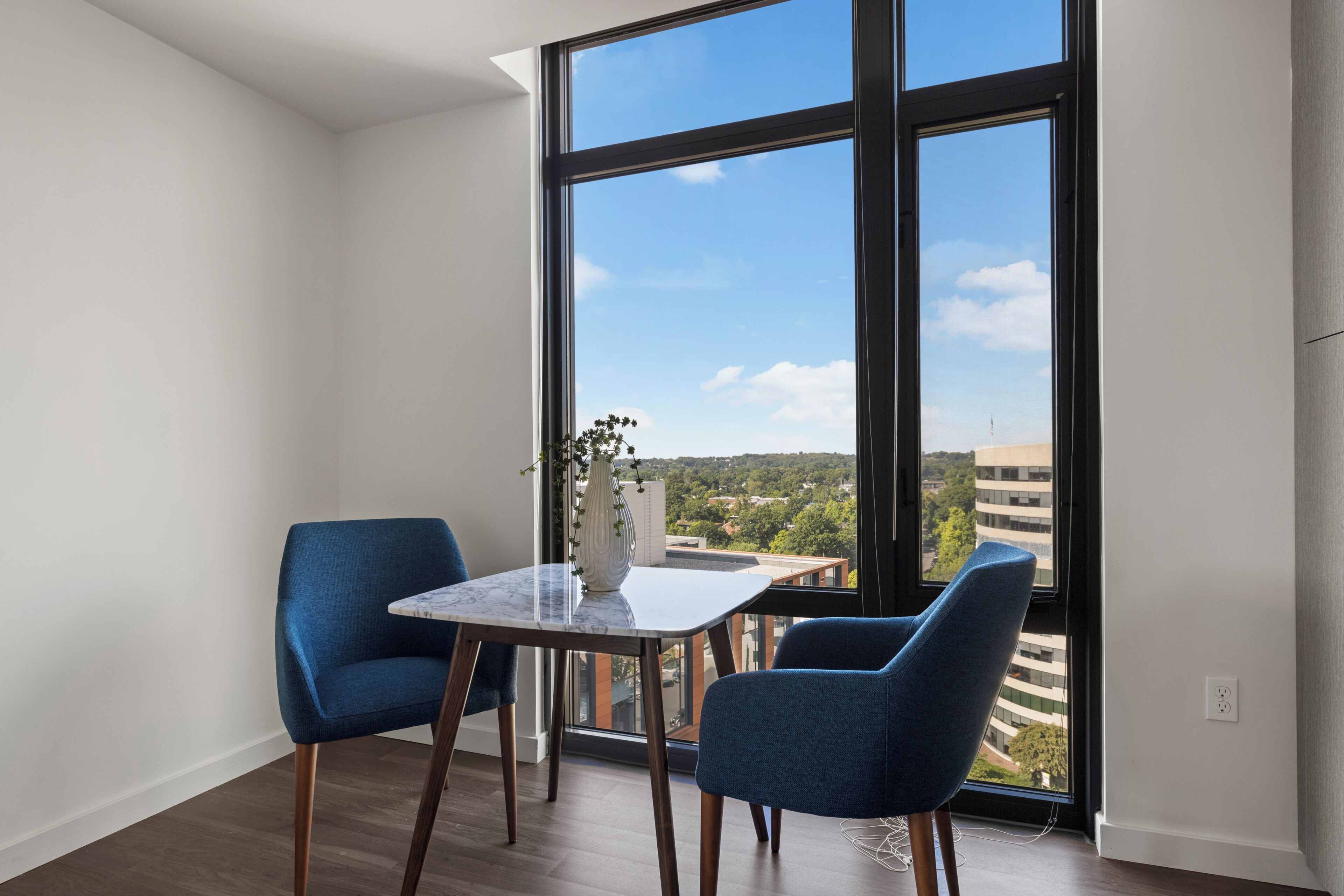 A room with a large window, two chairs, a small table, and a vase with flowers.