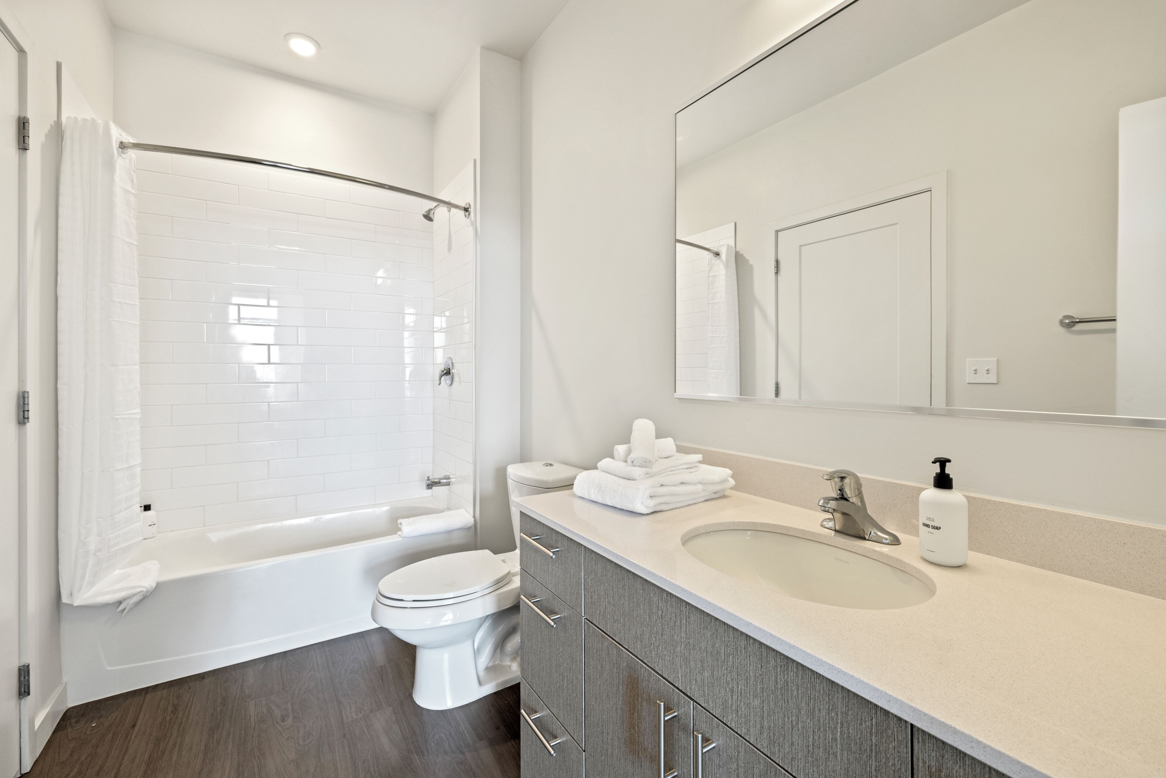 A modern bathroom with a shower, toilet, sink, and a mirror.