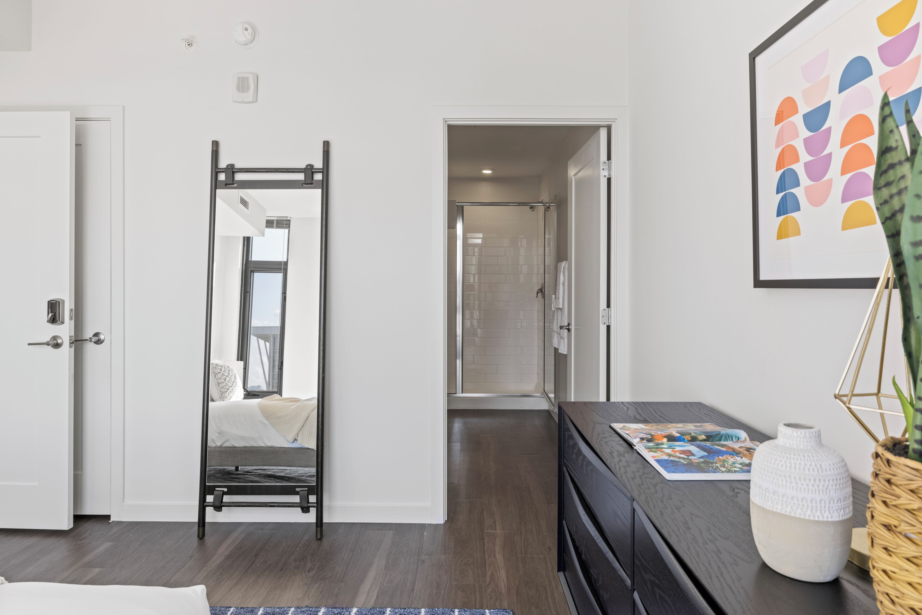 Habitació d'hotel moderna amb un llit, una taula de nit, un mirall, una obra d'art emmarcada i vistes al bany.
