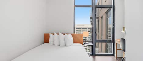 Una habitación de hotel moderna con una cama grande, un escritorio y vistas a la ciudad a través de un ventanal amplio.
