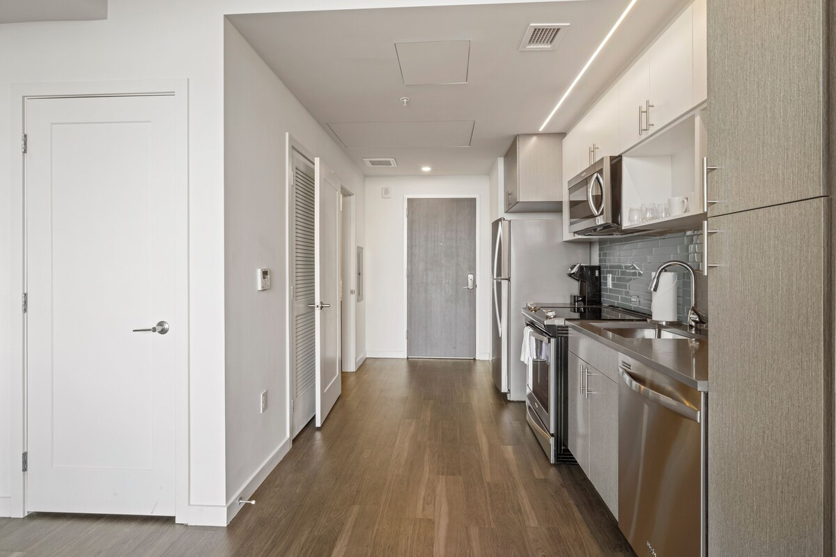A modern kitchen with stainless steel appliances, wooden flooring, and white cabinetry.