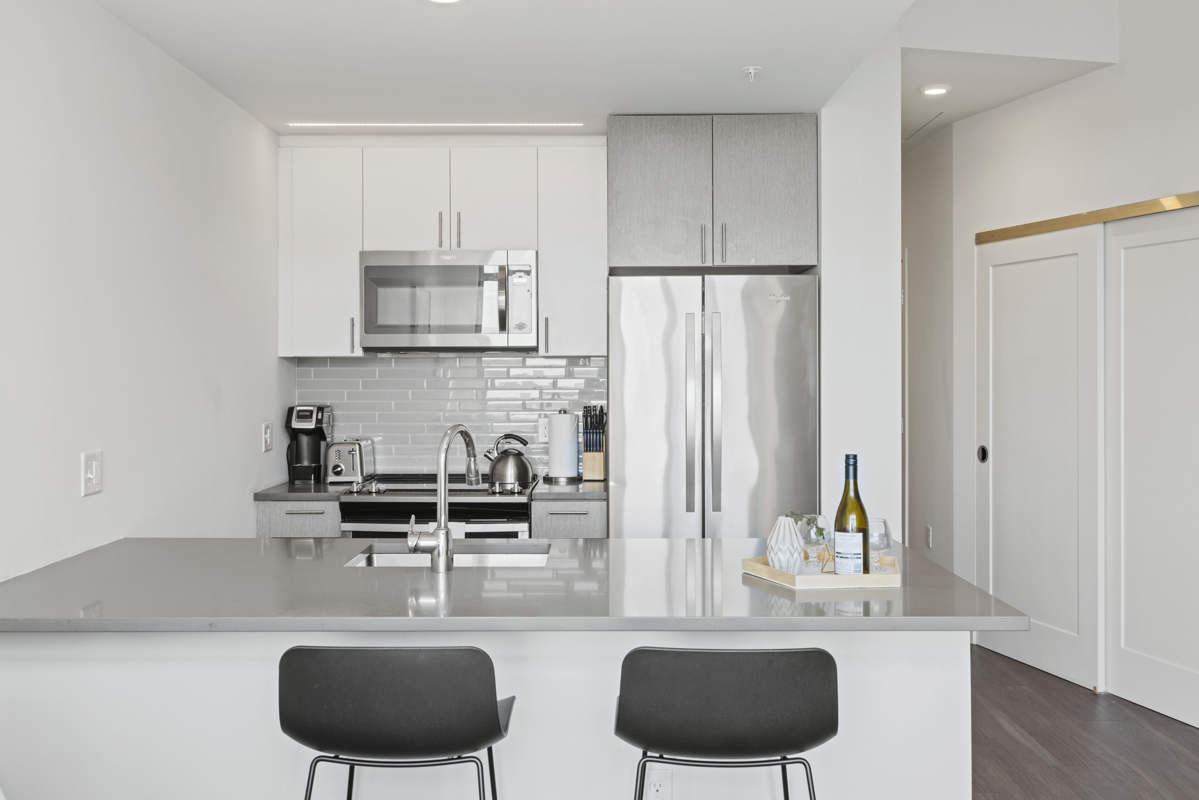 Une cuisine moderne avec des meubles blancs, des appareils en acier inoxydable et un îlot central doté de deux tabourets de bar.
