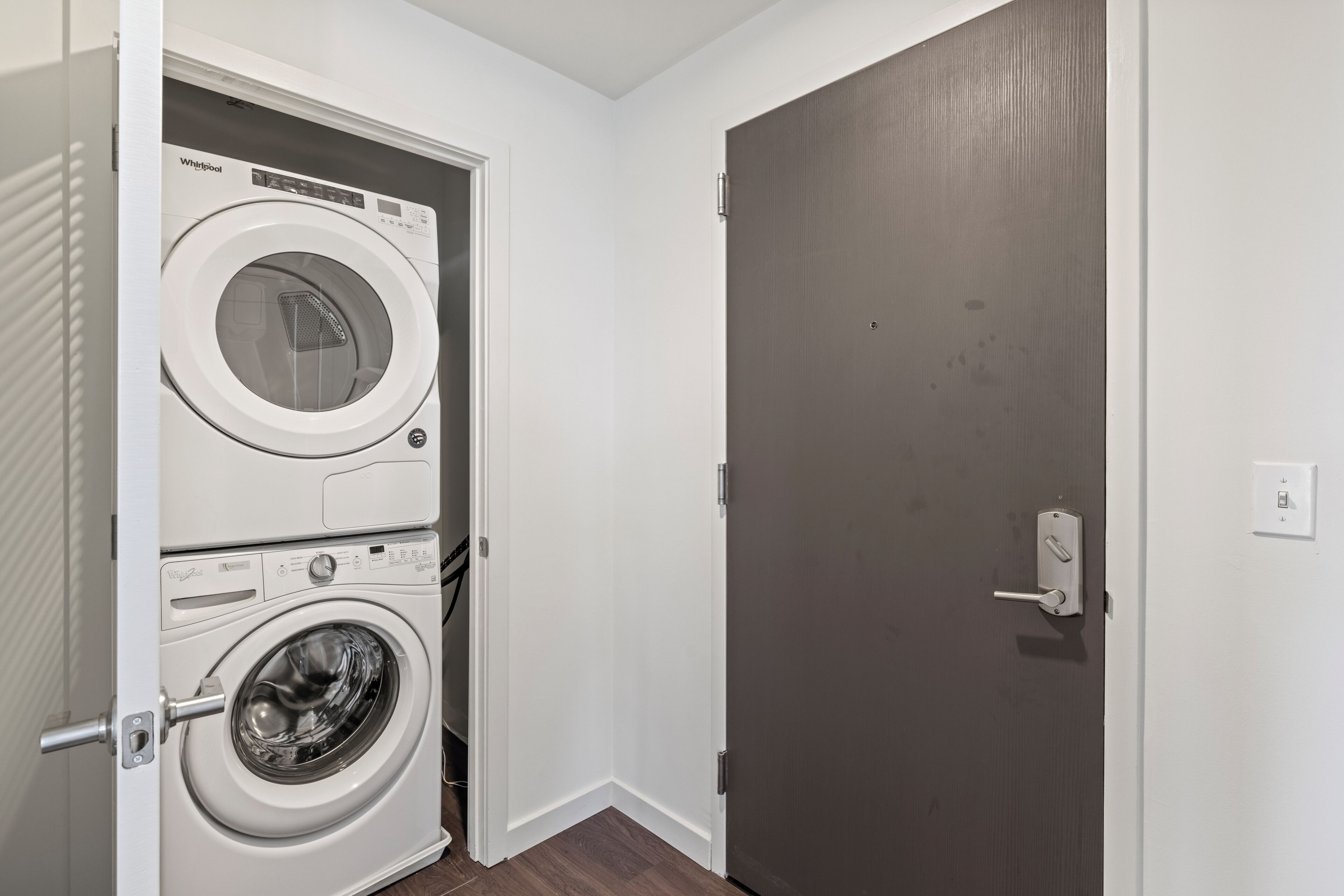 A laundry room with a front-loading Whirlpool washer and dryer, a door with a handle, and a light switch on the wall.