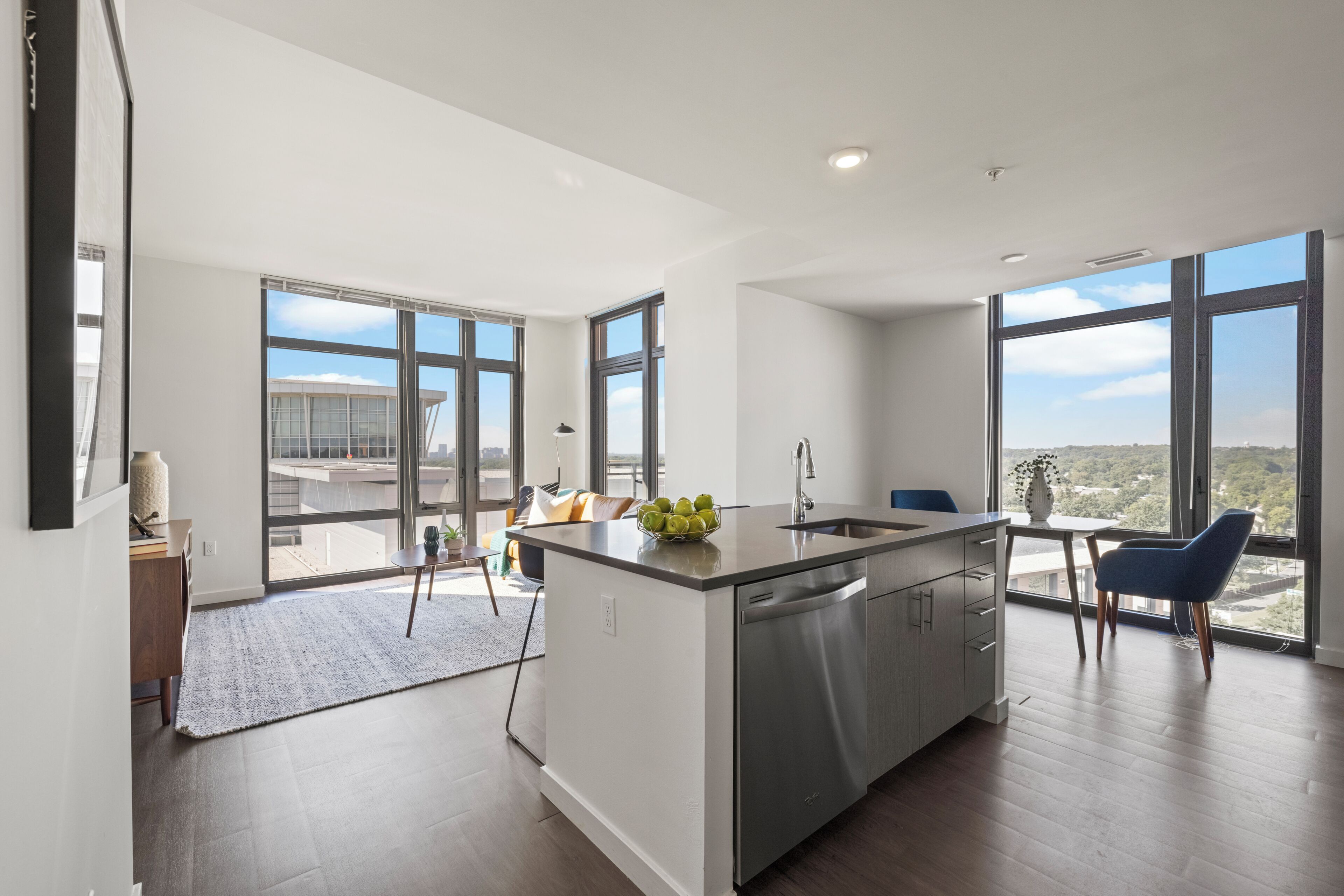 A modern kitchen with a large island, a dishwasher, and a view of the city through large windows.