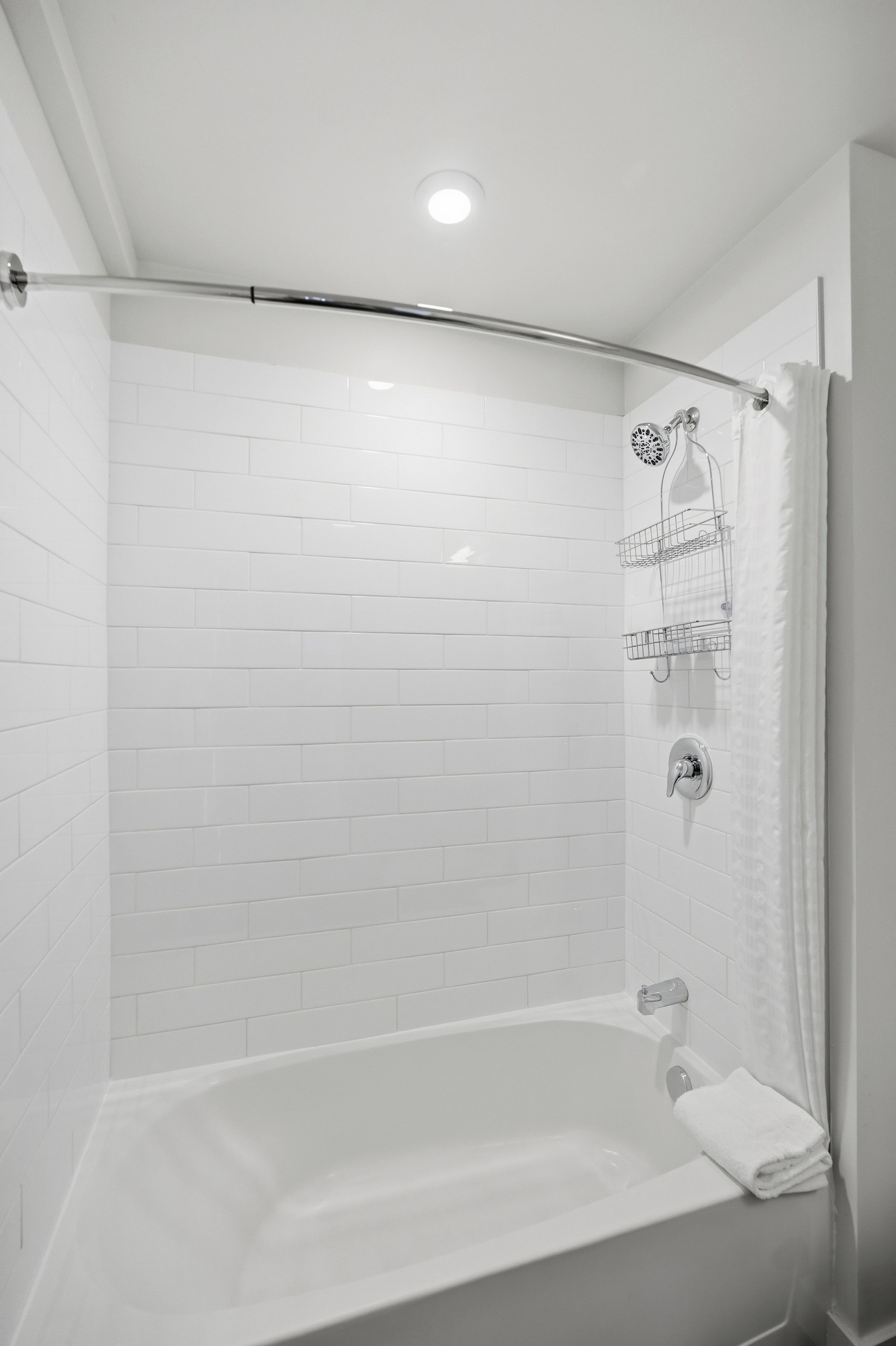 A modern bathroom with white tiled walls, a bathtub, a shower with a glass door, and a towel rack.