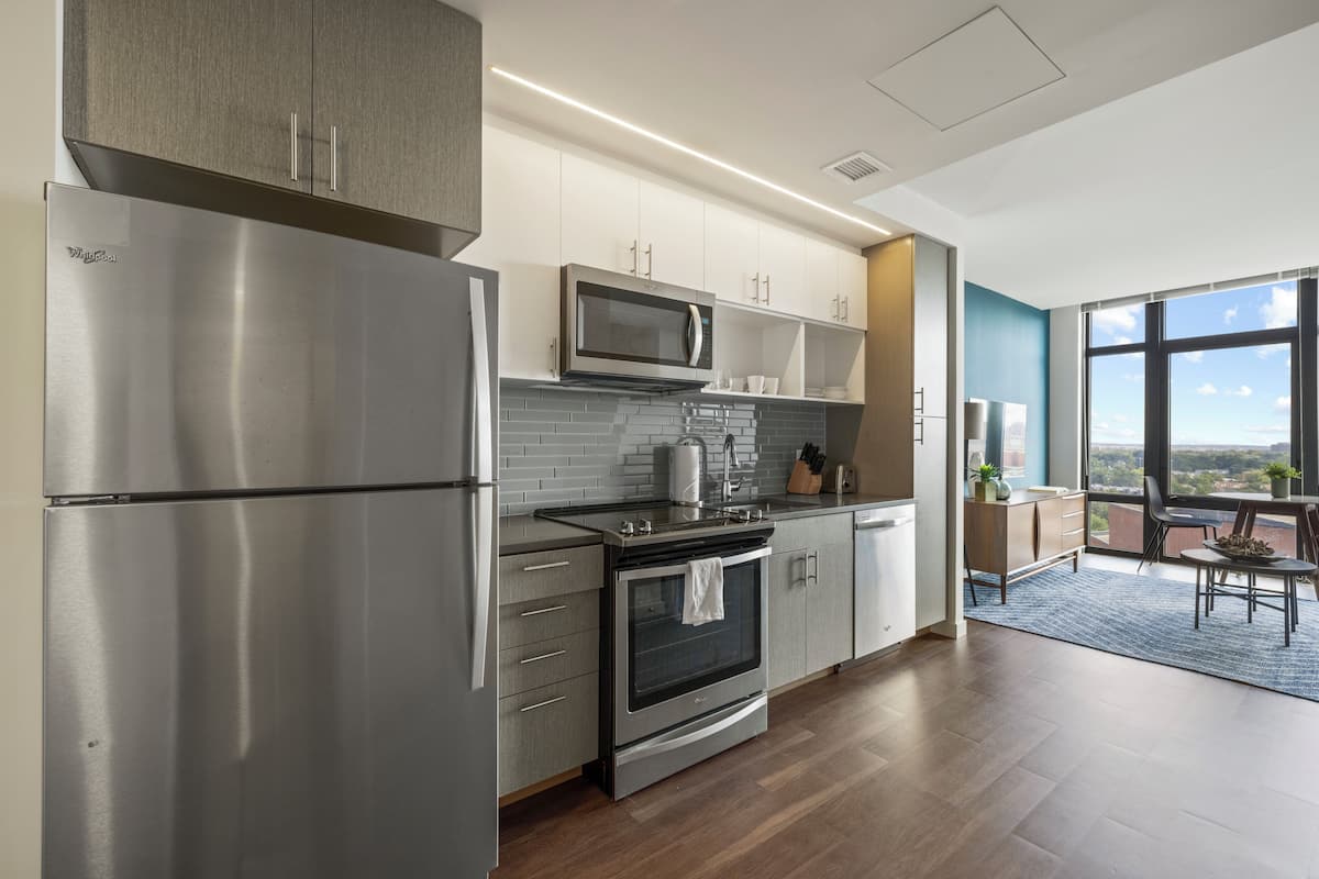 A modern kitchen with stainless steel appliances, a microwave, and a stove. There is a dining area with a table and chairs, and a large window offering a view.