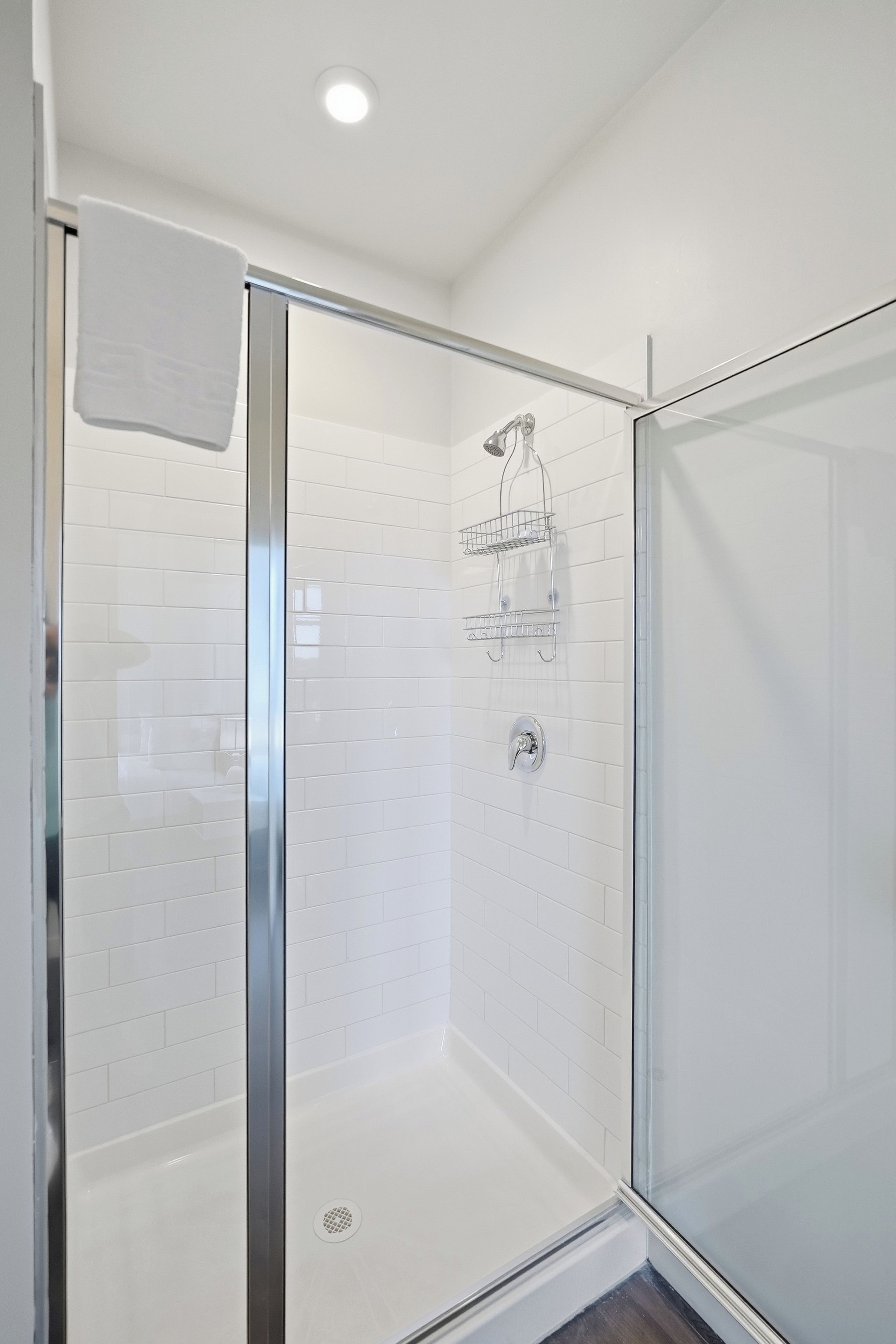 A glass-enclosed shower with white tiled walls and a glass door.