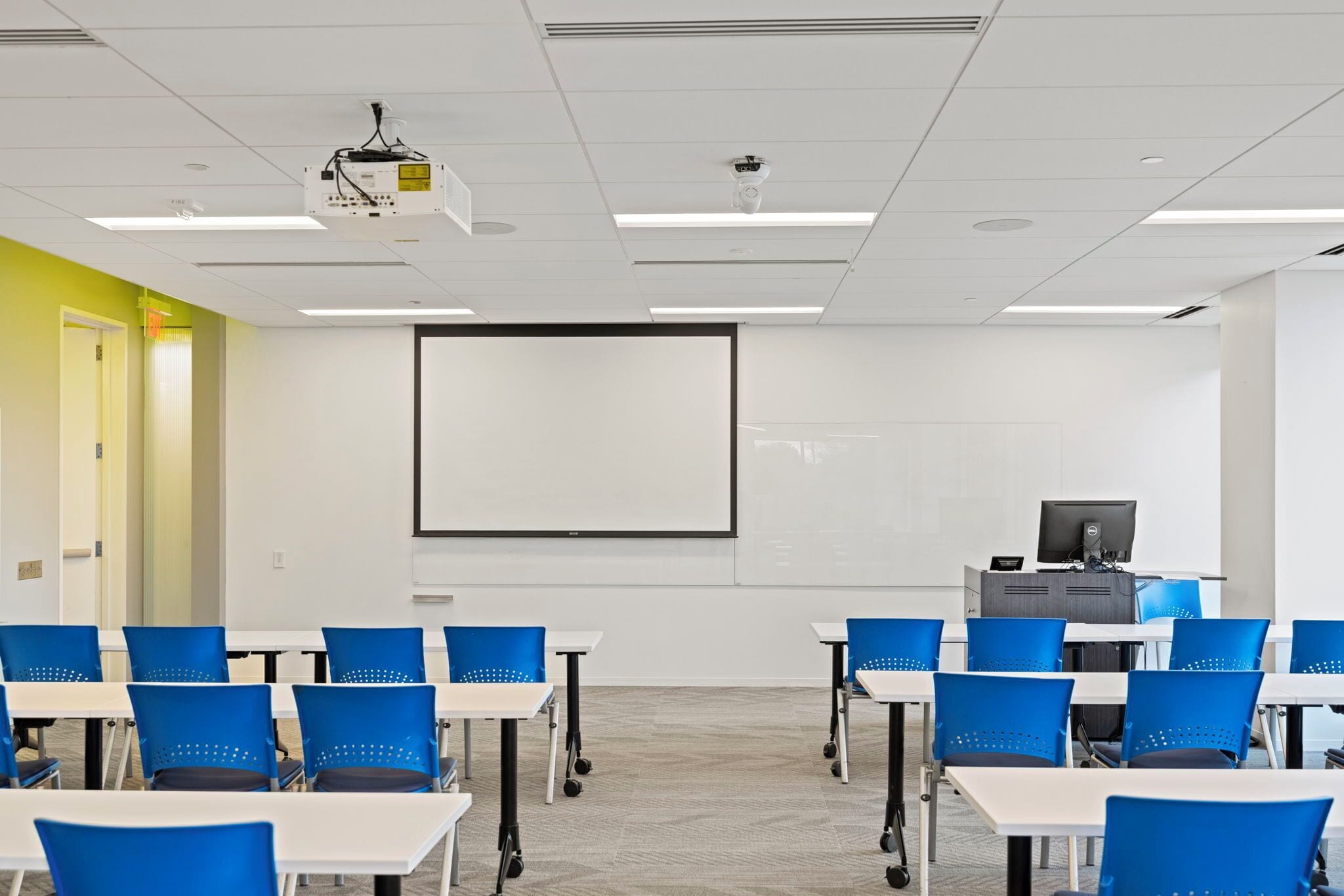 A conference room with white tables, blue chairs, a projector, and a screen.