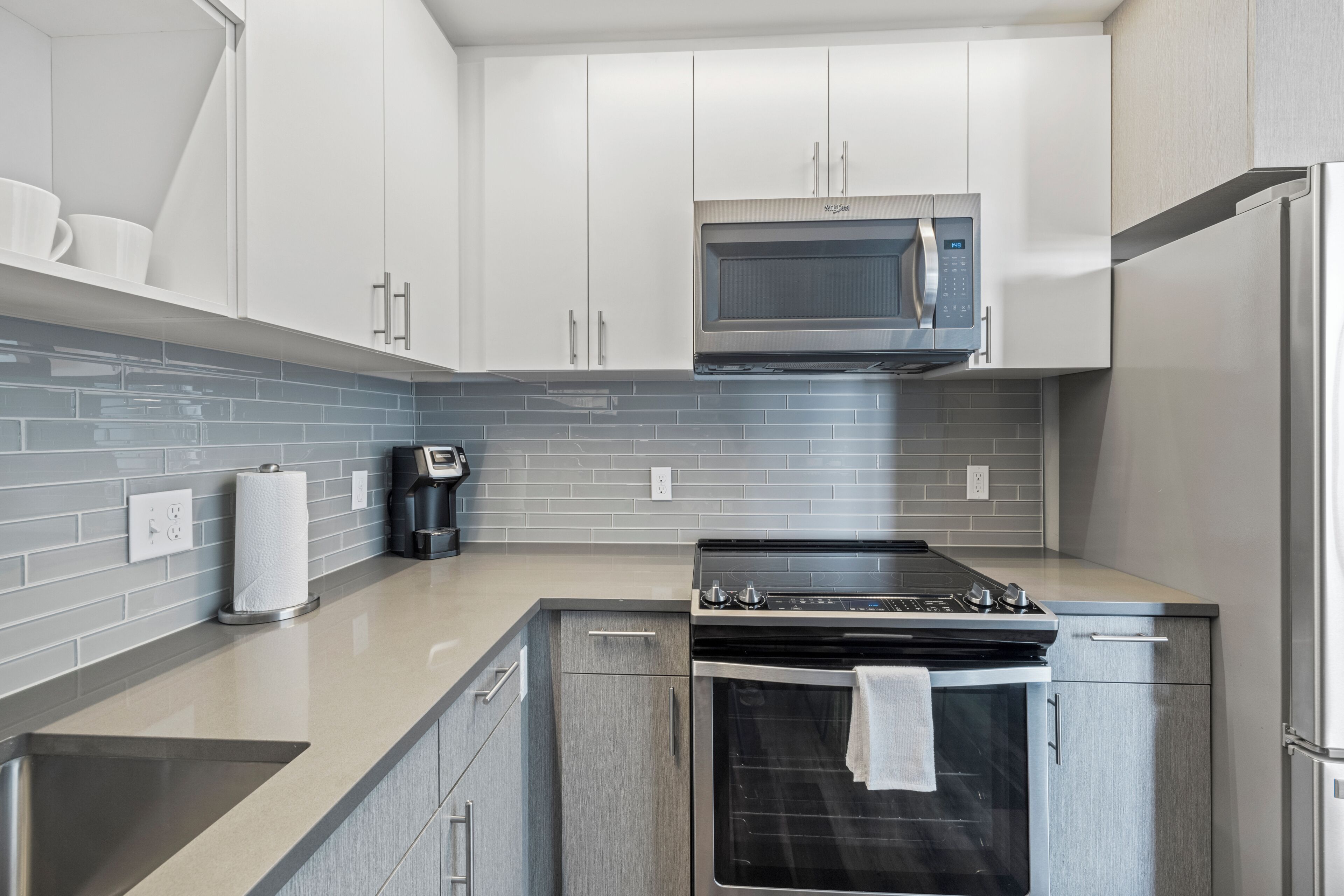 Una cocina moderna con armarios blancos, estufa de acero inoxidable, microondas y refrigerador.