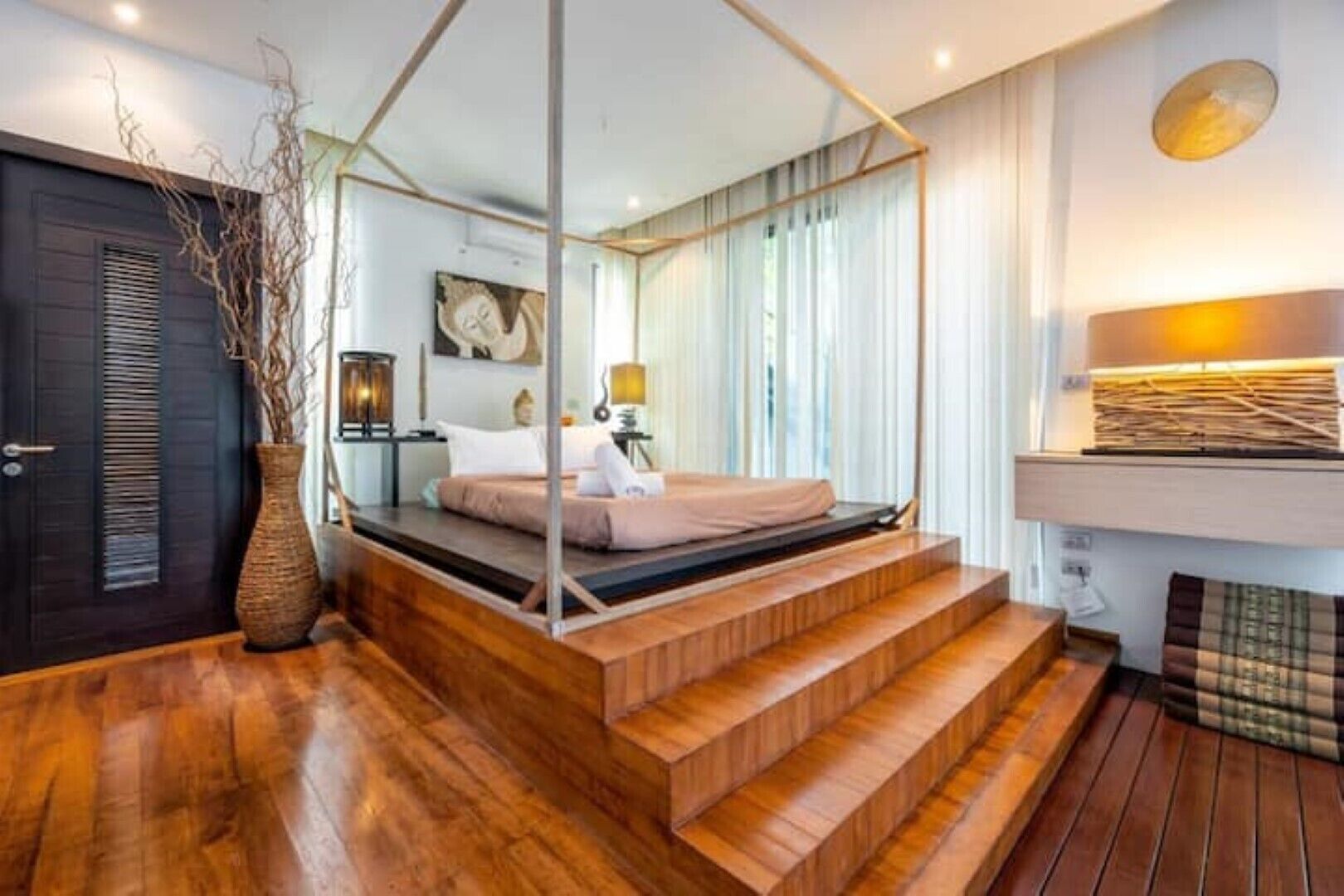 Een moderne slaapkamer met een houten vloer, een bed met hemelbed, een grote spiegel en een nachtkastje met een lamp.