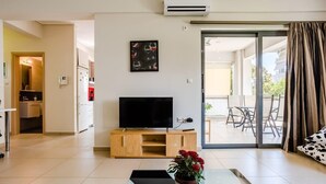 Ein modernes Wohnzimmer mit Fernseher, Couchtisch und Sofa. Ein großes Glasbild verschiebt sich zu einem Außenbereich mit Tisch und Stühlen.