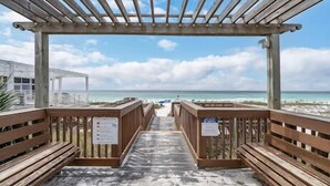 Ein Promenadweg am Strand mit Holzbanken und einer Pergola.