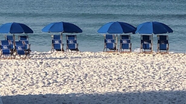 Ein Strand mit blauen Liegestühlen und Sonnenschirmen, einem sandigen Ufer und einem ruhigen Meer im Hintergrund.